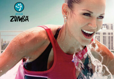 Eine Frau mit pinkem Oberteil die von einer kleinen Welle nass gemacht wird. In der linken oberen Ecke ist ein Schriftzug "Zumba" eingefügt.