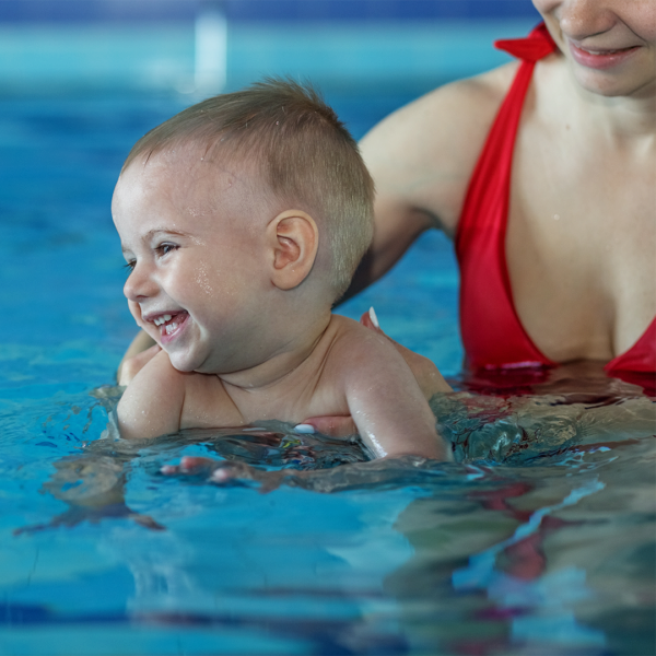 Ein Baby im Wasser, welches von seiner Mama gehalten wird.
